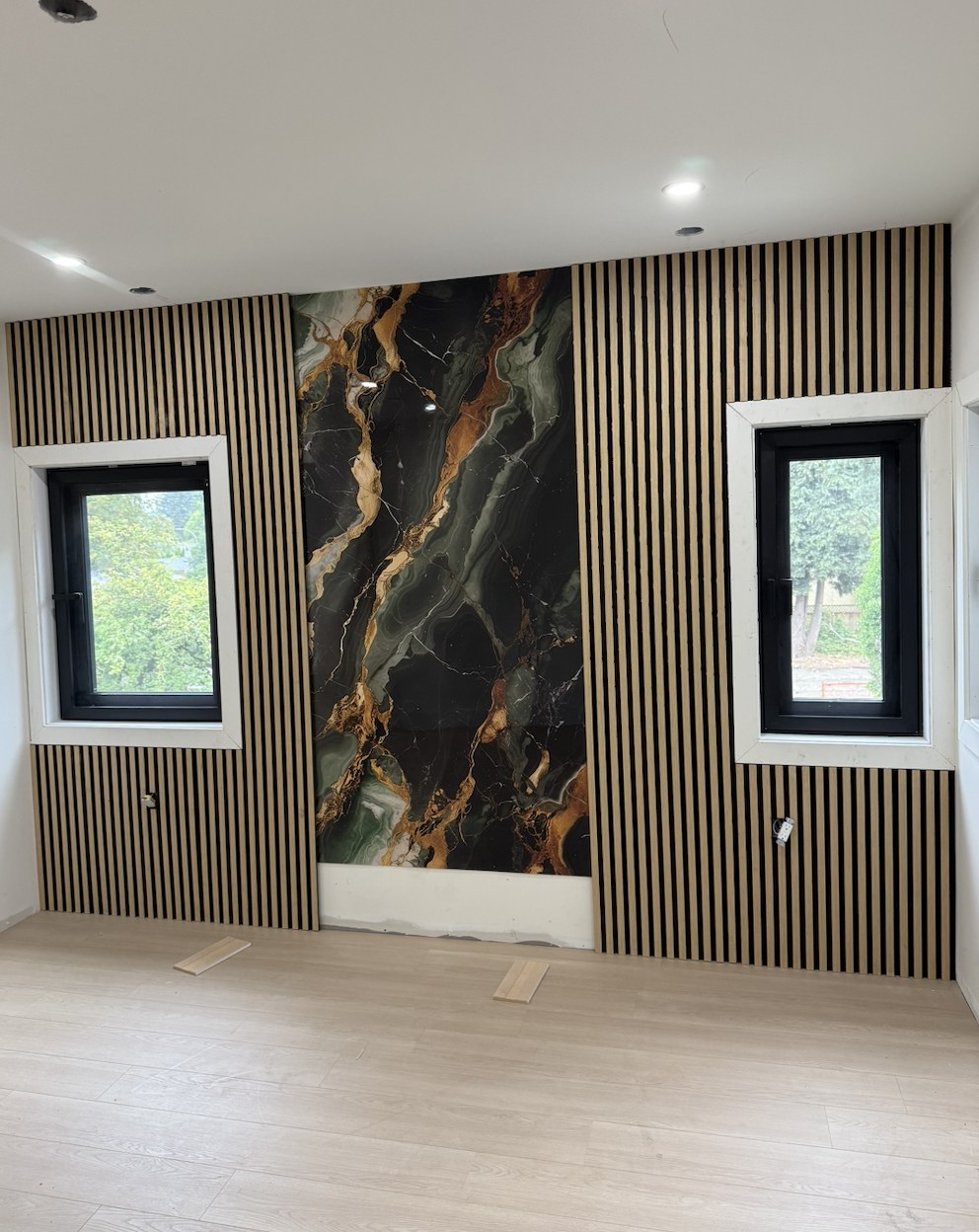 Oak slat feature wall with a dark marble panel above wide-plank flooring